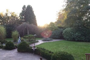 A garden with a stone pathway, neatly trimmed hedges, and a variety of trees and shrubs.