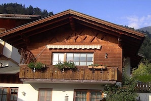 A wooden chalet with a balcony, a window with curtains, and a mountain backdrop. - Holiday apartment with 1 bedroom (Garmisch-Partenkirchen)