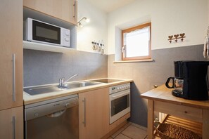 Eine kompakte Küche mit Mikrowelle, Backofen, Geschirrspüler und einer Kaffeemaschine auf einem kleinen Tisch.