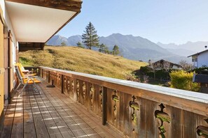 Eine Holzterrasse mit Geländer, mit Blick auf eine hügelige Landschaft und Berge im Hintergrund.