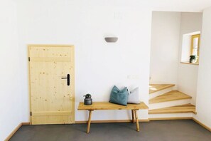 Quarto minimalista com porta de madeira, um pequeno banco com almofadas e uma escada.