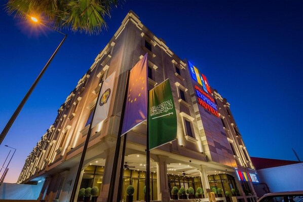 A multi-story hotel with a prominent flag display, a well-lit entrance, and a modern architectural design. - Ewaa Express Hotel - Gaber Riyadh (Riyadh)