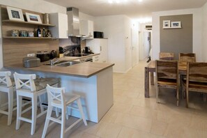 A modern kitchen with a central island, bar stools, and a dining table with wooden chairs. - Seaside magic by the sea (Norddeich)