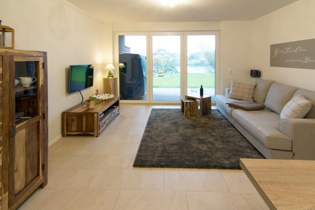 A living room with a sofa, a television, a wooden cabinet, and a large sliding glass door leading to a garden.