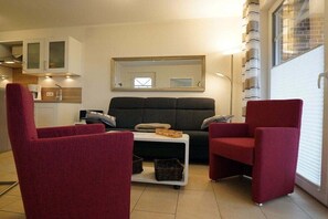 A living room with a sofa, two armchairs, a coffee table, and a kitchen area with cabinets and a mirror. - Holiday apartment with 2 bedrooms (Norddeich)