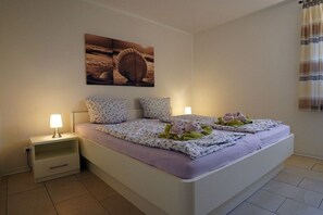 Une chambre à coucher comprenant un lit, des tables de chevet, une œuvre d’art accrochée au mur et une fenêtre avec des rideaux.