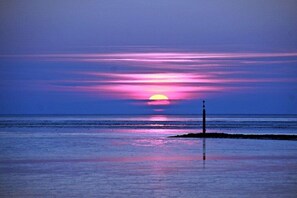 Un coucher de soleil sur une mer calme, avec un seul poteau au premier plan.