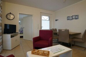 A living room with a television, a red armchair, a dining table with chairs, and a 'HOME' sign on the wall. - Holiday apartment with 2 bedrooms (Norddeich)