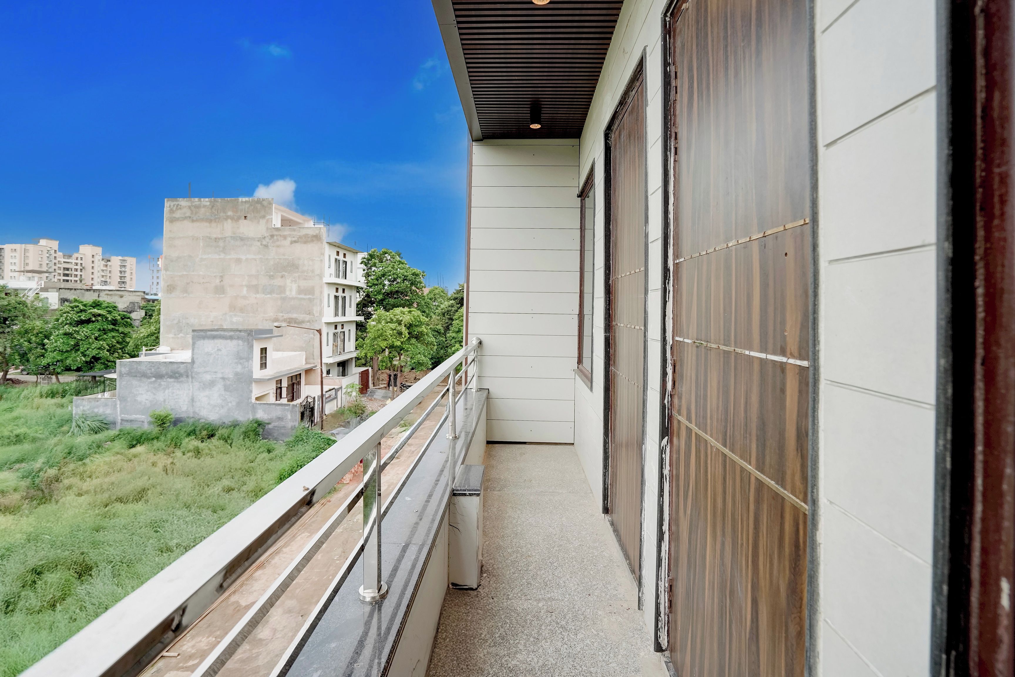 Un balcón con vista a una zona residencial, una estructura de concreto y un edificio con puerta de madera.