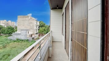 Un balcón con vista a una zona residencial, una estructura de concreto y un edificio con puerta de madera.