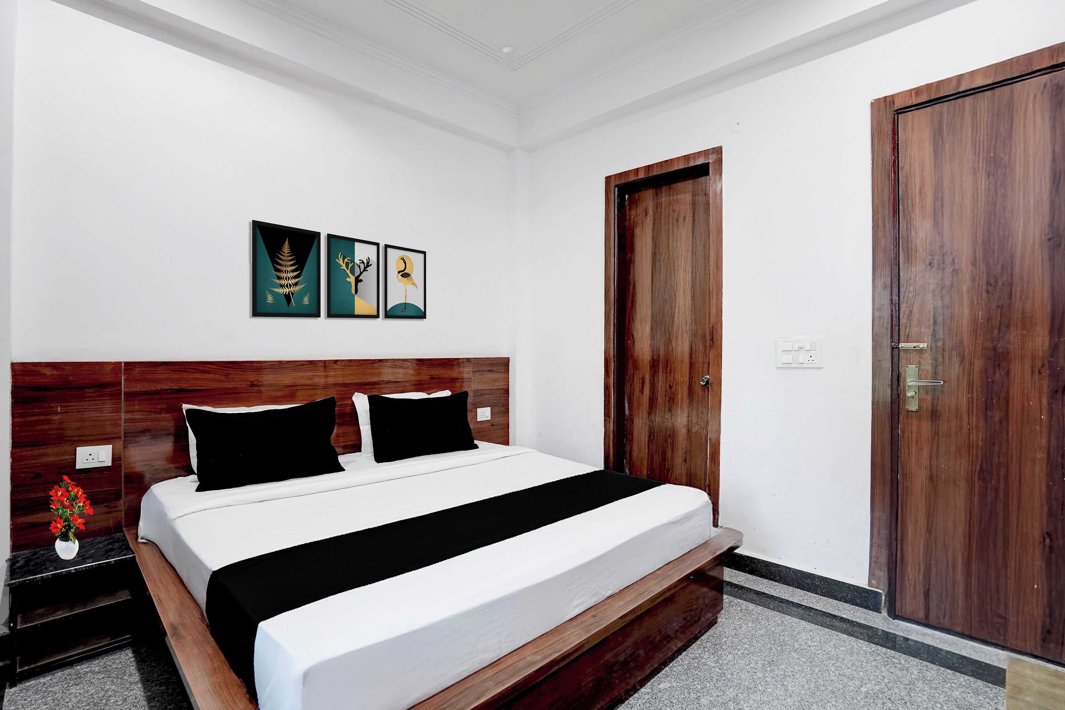 Una habitación de hotel con cabecera de madera, cama con ropa de cama blanca y negra, y una puerta con marco de madera.