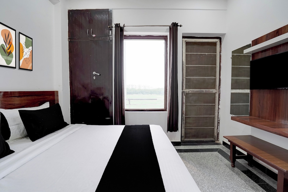Habitació d'hotel amb un llit, una banca, un televisor, una porta i una finestra.