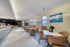 A modern dining area with multiple tables and chairs, a kitchen counter, and a wall-mounted menu board. - Jinjiang Inn Select (Shanghai)