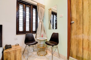 Una habitación con dos sillas negras, una mesita, un armario de madera, un teléfono y una ventana con cortinas.