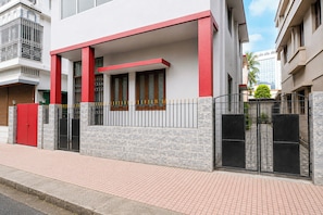 A modern building with a red and white facade, a gated entrance, and a paved sidewalk. - Collection O Vaisaakkhi Mall Salt Lake (Barasat)