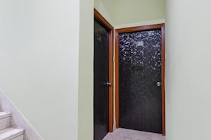 Un pasillo con una puerta oscura marcada con el número 203, una escalera de mármol y una pared lisa.