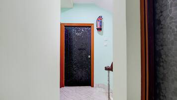 A hallway with a tiled floor, a door with a number sign, a fire extinguisher, and a wall with a textured pattern.