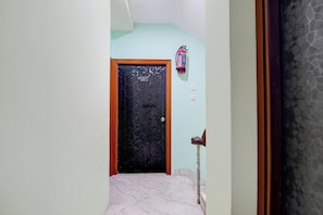 A hallway with a tiled floor, a door with a number sign, a fire extinguisher, and a wall with a textured pattern. - Collection O Vaisaakkhi Mall Salt Lake (Barasat)