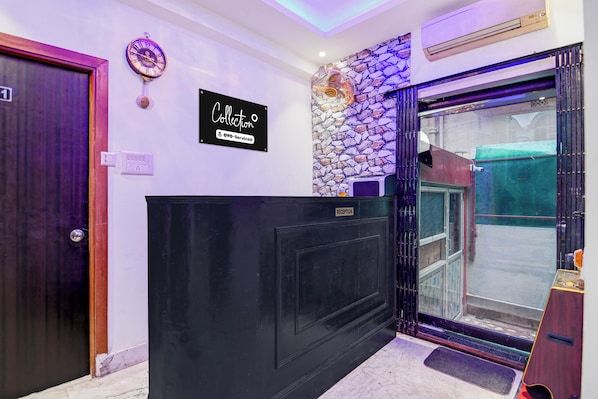 A reception area with a black reception desk, a clock, and a sign indicating 'Collection OYO-Serviced'. - Collection O Vaisaakkhi Mall Salt Lake (Barasat)