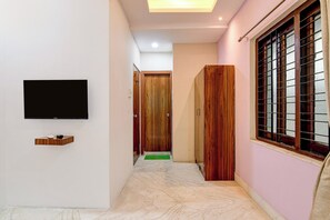 Corredor com televisão de tela plana na parede, porta de madeira e janela com grades de metal.