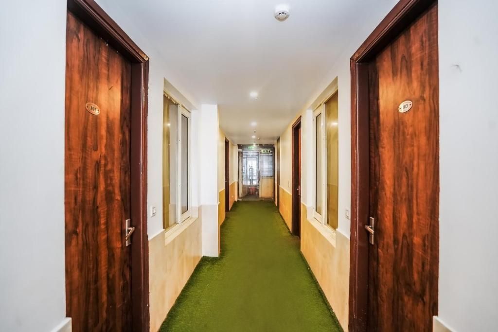 A hallway with wooden doors, a green carpet, and a white wall.