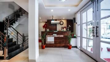 A reception area with a wooden desk, potted plants, a staircase, and a large window with a view of the outside.