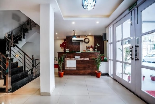 Un área de recepción con un escritorio de madera, plantas en macetas, una escalera y un ventanal con vistas al exterior.