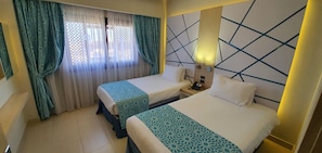 Habitación de hotel con dos camas, una ventana con cortinas translúcidas, una mesita de noche con teléfono y un diseño geométrico en la pared.
