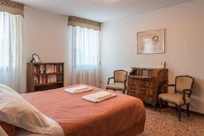 A hotel room with a bed, two chairs, a wooden dresser, a bookshelf, and a framed picture on the wall. - Ca Magno (Venice)