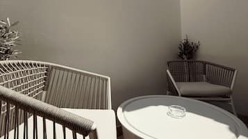 Un petit espace extérieur aménagé avec deux chaises en osier et une table ronde, entouré d’un mur sobre et d’un ciel dégagé.