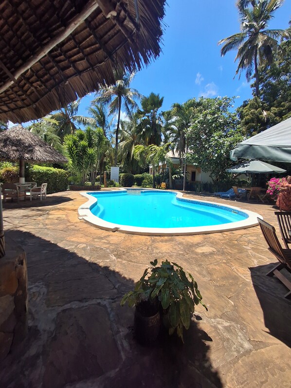 A swimming pool surrounded by palm trees and a thatched roof structure.