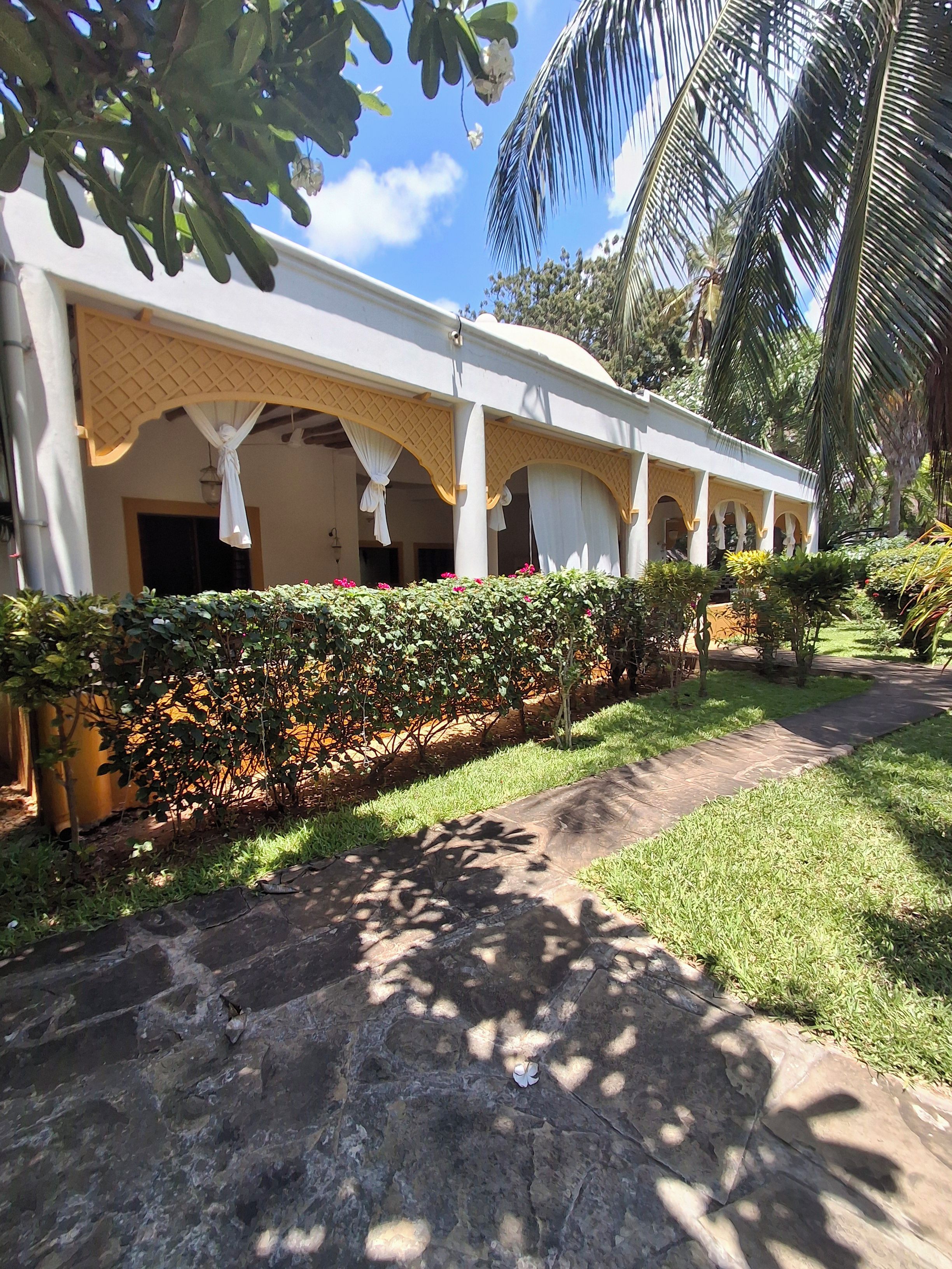 A building with a covered outdoor area, a stone pathway, and a well-maintained garden with various plants.