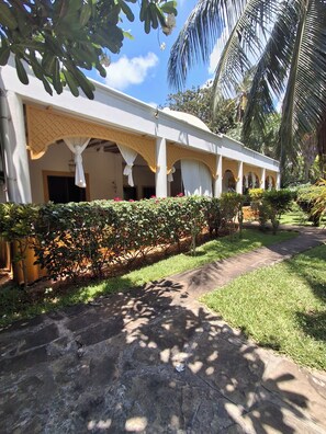 A building with a covered outdoor area, a stone pathway, and a well-maintained garden with various plants.
