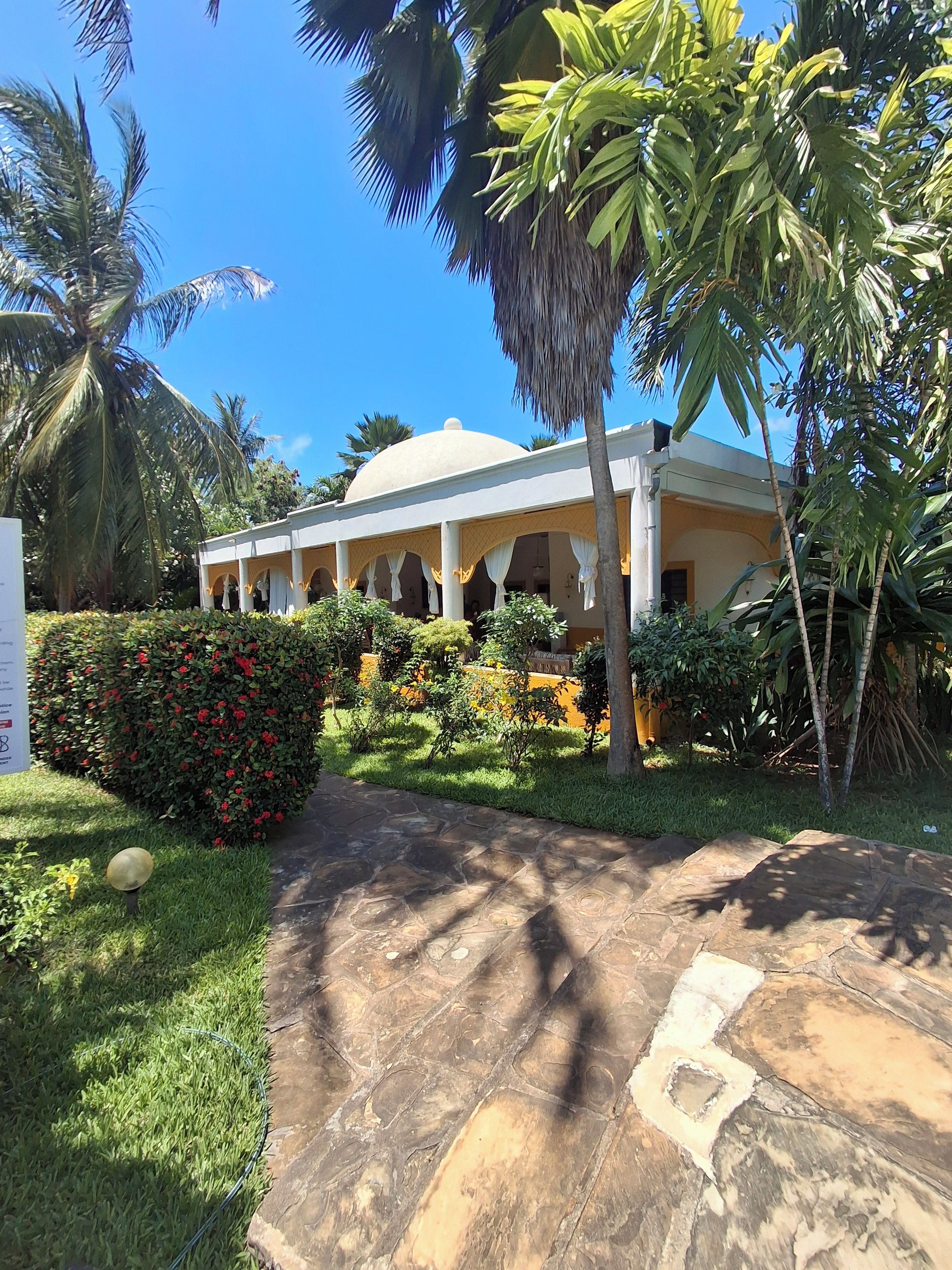 A building with a dome roof, surrounded by lush greenery and palm trees.