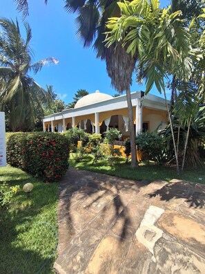 A building with a dome roof, surrounded by lush greenery and palm trees.