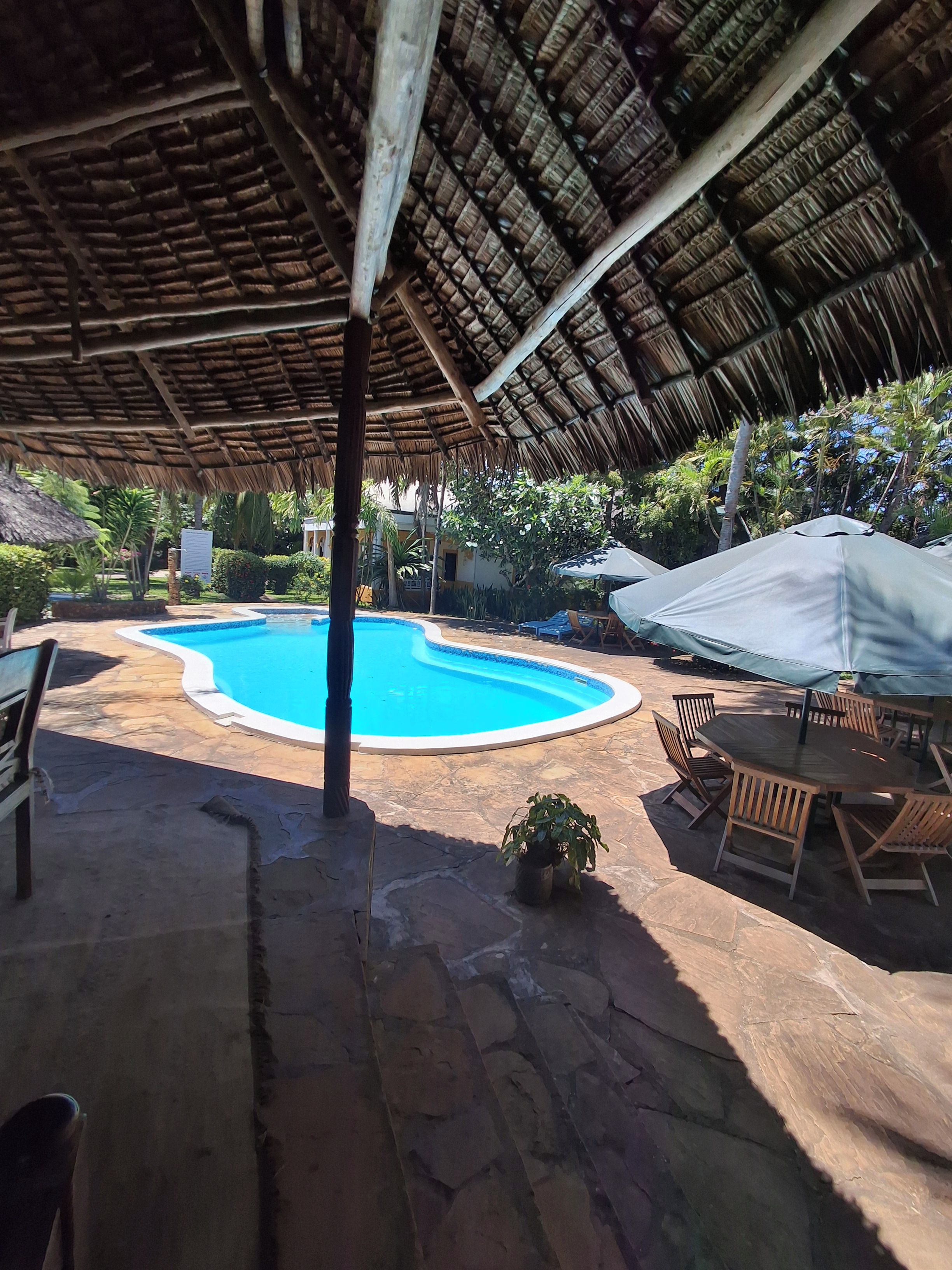 Un espace piscine doté d’un toit de chaume, d’un sol en pierre et de mobilier en bois.