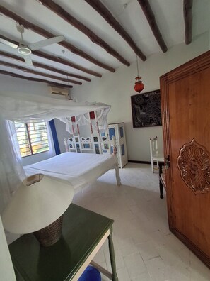 A room with a bed, a wooden door, a white wall, a ceiling fan, and a window.