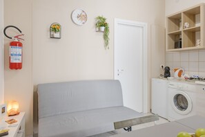 Ein gemütlicher, kleiner Wohnraum mit Bett, Waschmaschine und einer kleinen Küchenzeile.