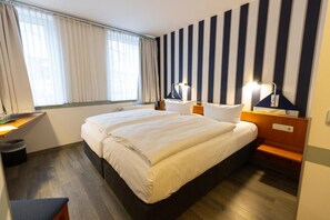 Habitación de hotel con cama doble, mesitas de noche, escritorio y ventana con cortinas.