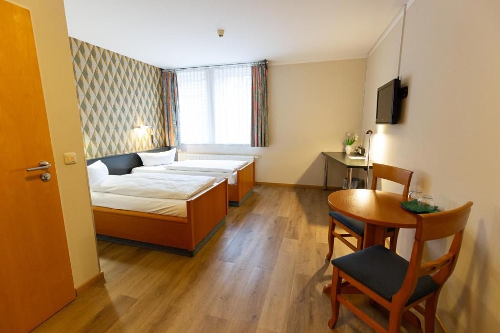 A hotel room with two beds, a desk, a chair, and a TV.