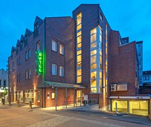 Un hotel moderno con un llamativo letrero verde, un acceso cubierto y un ascensor visible.