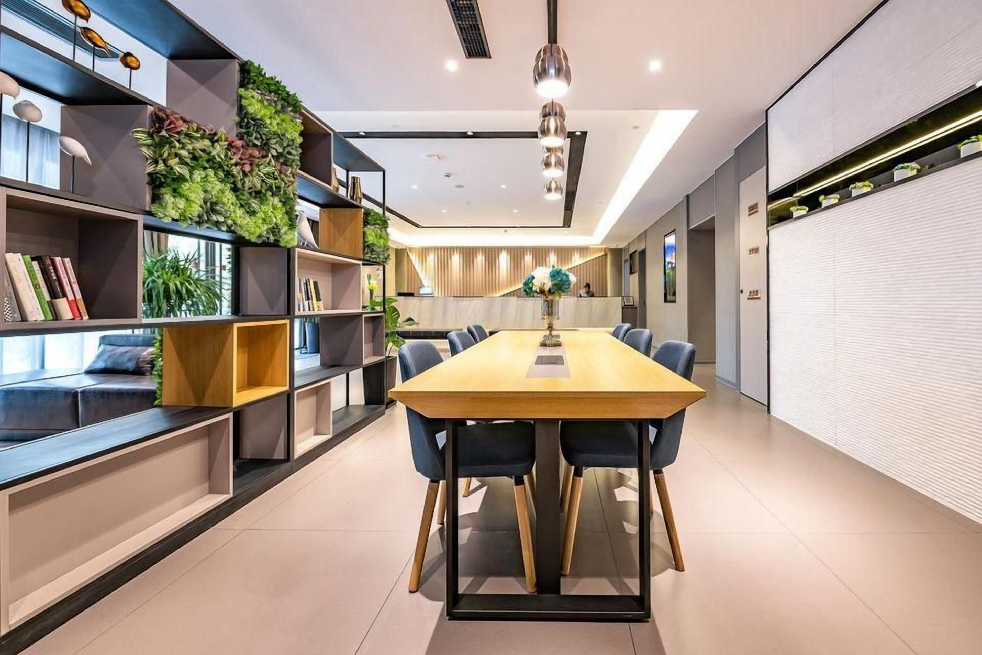 Ein modernes Interieur mit einem langen Esstisch, blauen Stühlen und verschiedenen Regalen mit Pflanzen und Büchern.