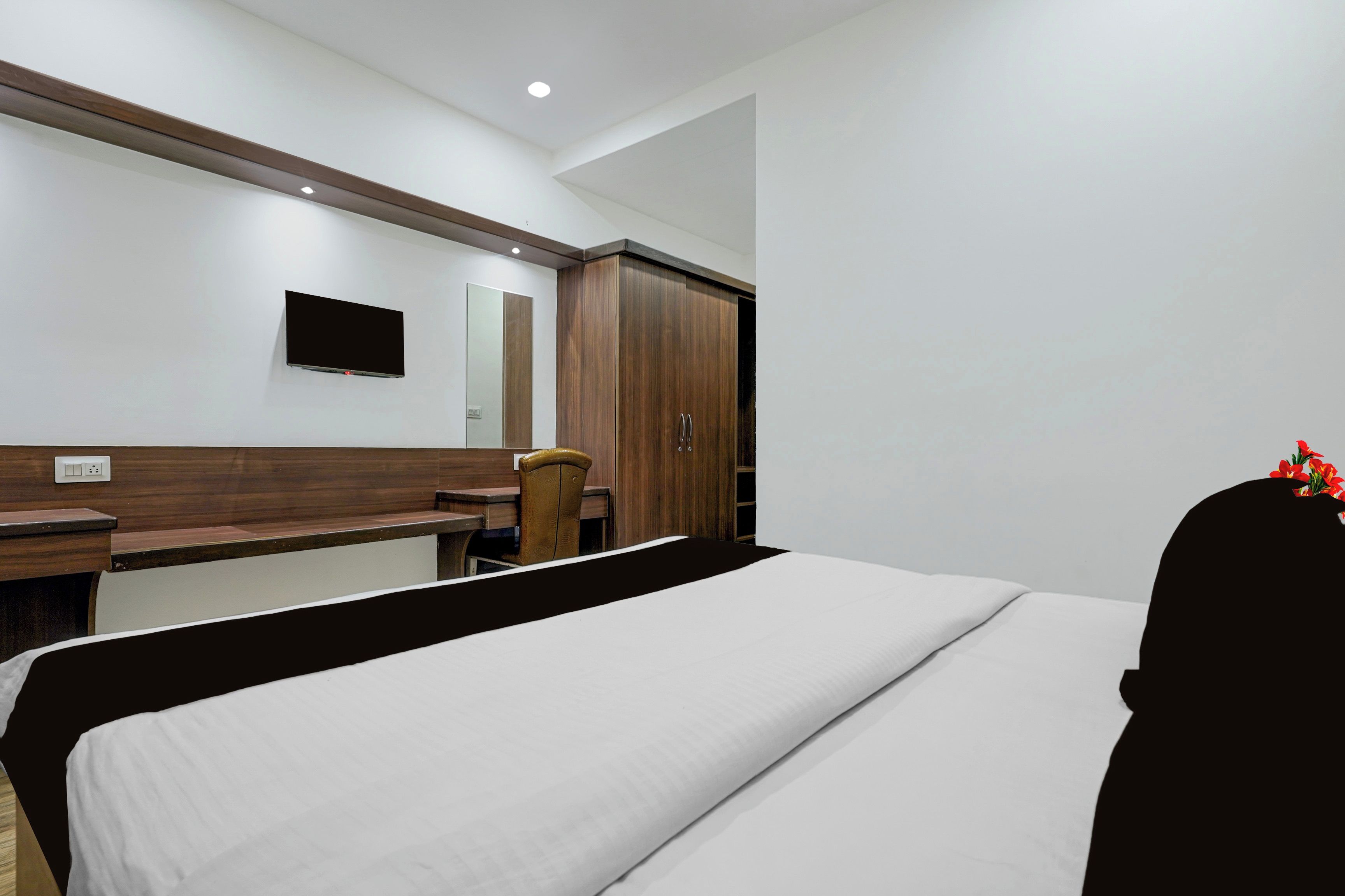 A hotel room with a bed, a desk, a chair, a wardrobe, and a television mounted on the wall.