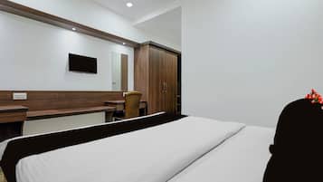 Habitación de hotel con cama, escritorio, silla, armario y televisor montado en la pared.