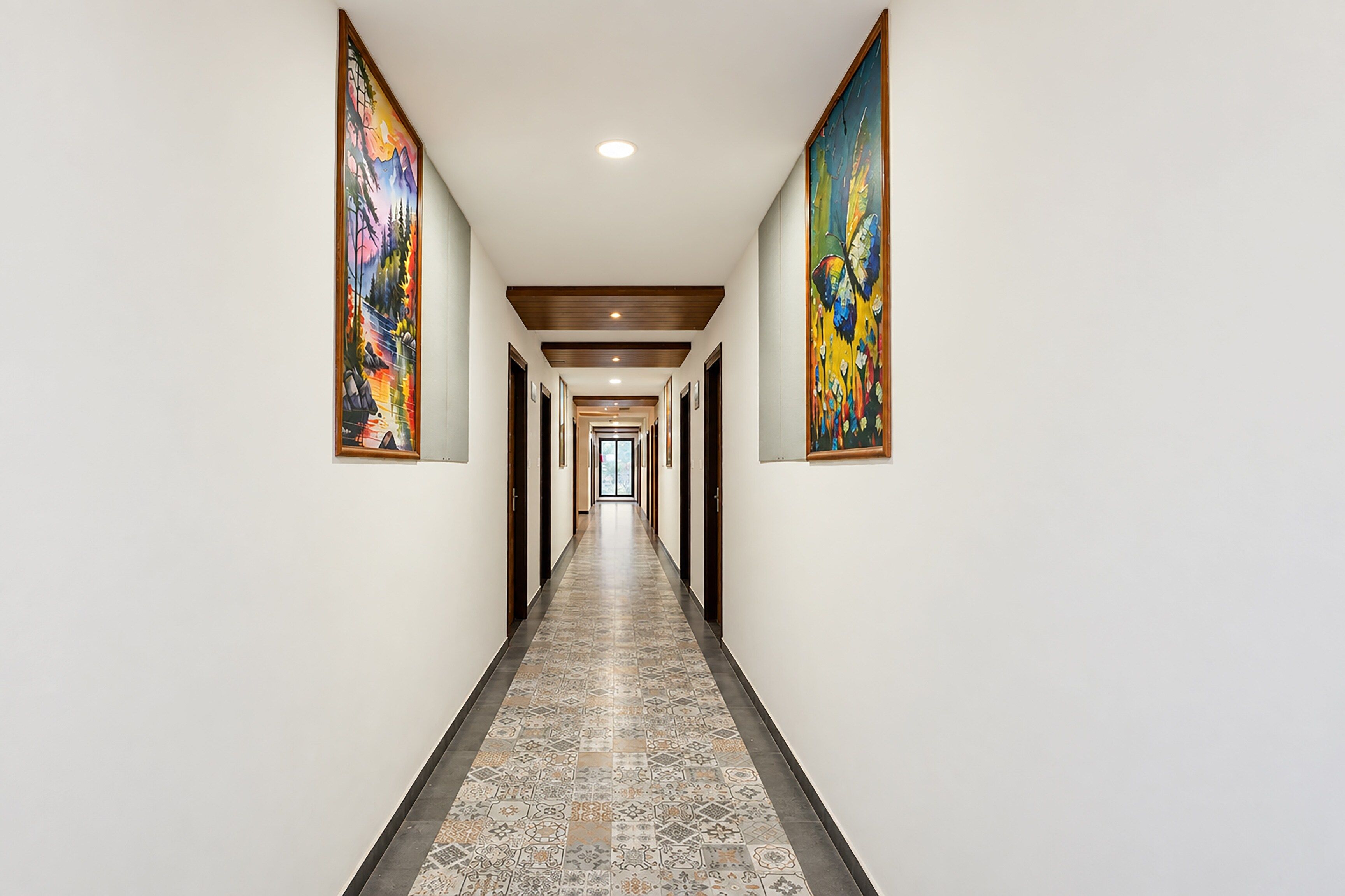 A long, narrow hallway with a patterned floor, flanked by two large paintings on the walls.
