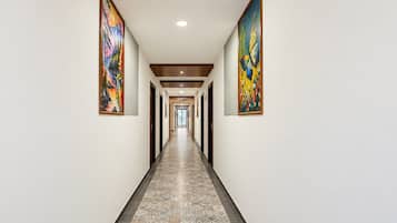 A long, narrow hallway with a patterned floor, flanked by two large paintings on the walls.