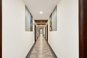 Un pasillo largo y estrecho con piso estampado, flanqueado por paredes con cuadros enmarcados.