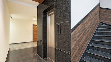 Un interior moderno con piso de piedra pulida, una escalera de madera y un ascensor.