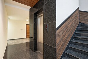 Un interior moderno con piso de piedra pulida, una escalera de madera y un ascensor.