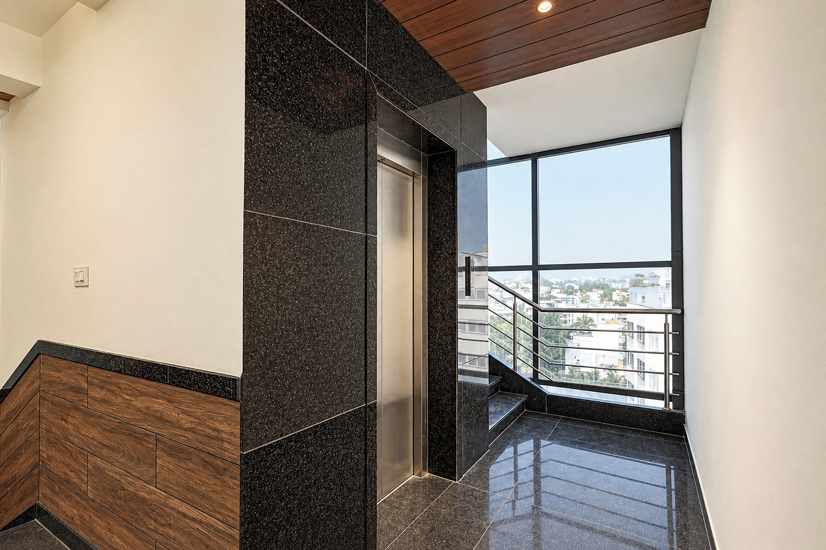 Un ascensor moderno con puerta de cristal, suelo de madera y vistas a un paisaje urbano a través de amplios ventanales.